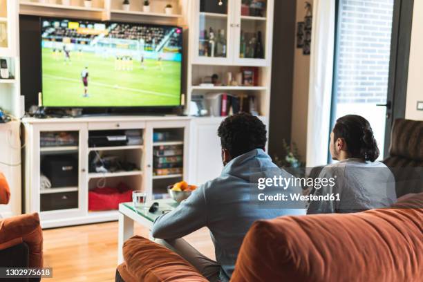 young male friends playing soccer game on television in living room at home - young men playing soccer stock pictures, royalty-free photos & images