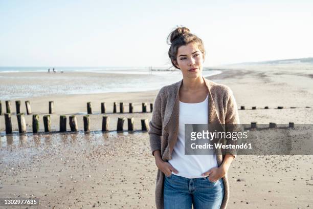 young woman with hands in pockets looking away at beach - young woman standing against clear sky ストックフォトと画像