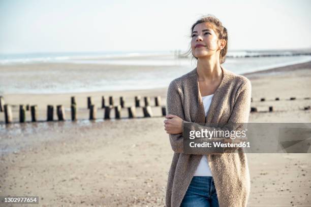 young woman looking up with arms crossed at beach - young woman standing against clear sky stock pictures, royalty-free photos & images