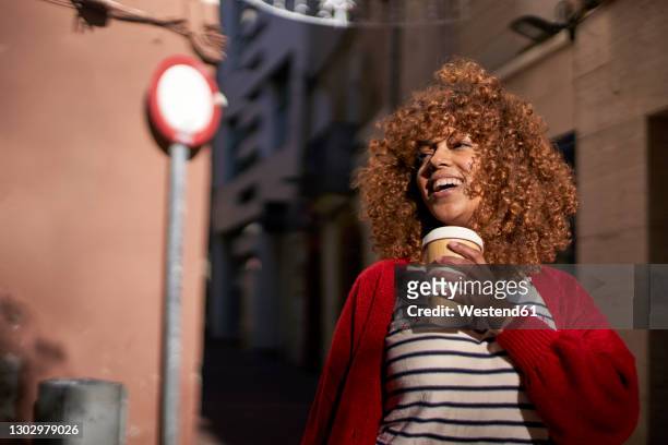 smiling woman with disposable coffee cup looking away while standing outdoors - coffe to go stockfoto's en -beelden