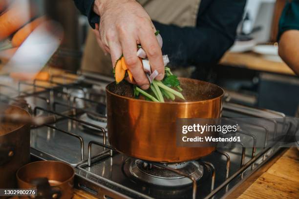 chef putting vegetables in copper saucepan while making broth soup in kitchen - make stockfoto's en -beelden