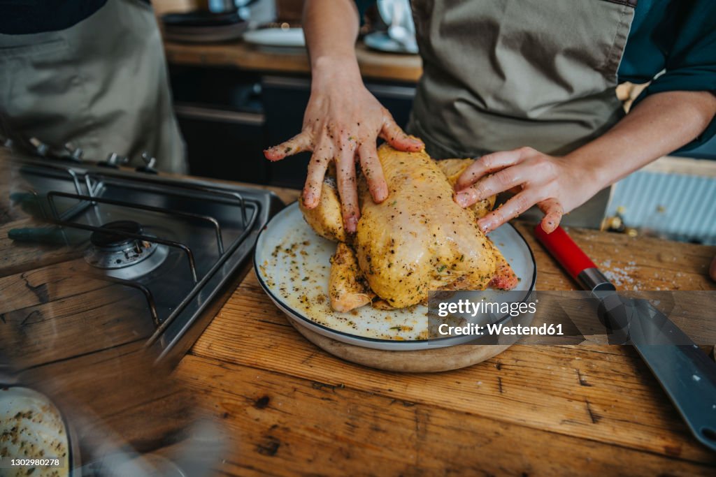 Chef marinating chicken meat while standing by colleague in kitchen