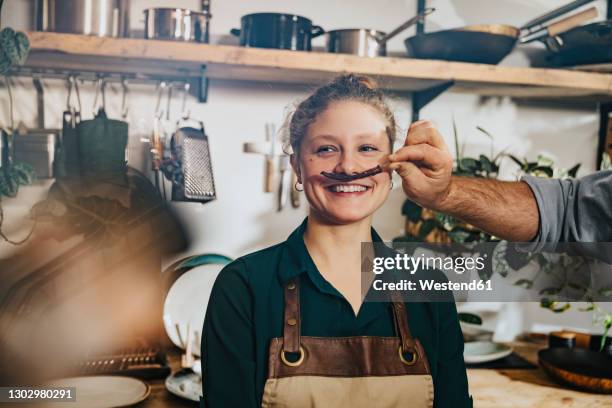 chef making mustache of dry chili to colleague while standing in kitchen - chili woman fotografías e imágenes de stock