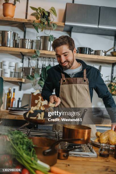 smiling male chef tossing mushroom in frying pan while standing in kitchen - cooked mushrooms stock pictures, royalty-free photos & images