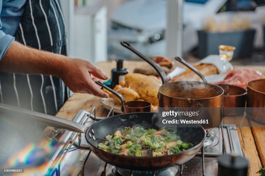 Male expertise cooking king oyster mushroom and scallions in frying pan while standing in kitchen