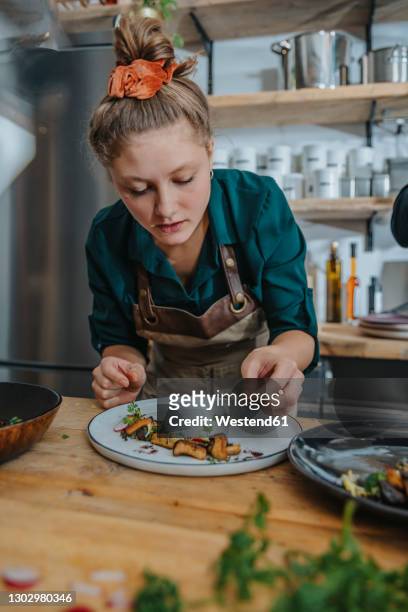 young female chef garnishing dish while standing in kitchen - finishing food stock pictures, royalty-free photos & images