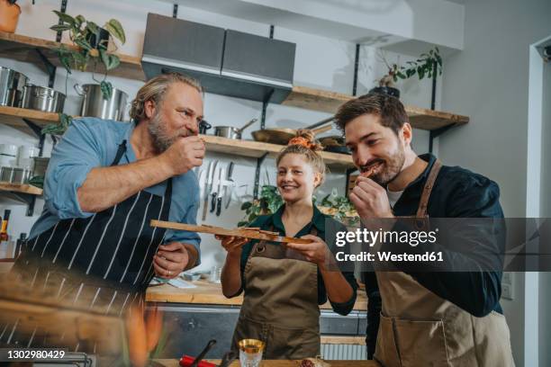 male chefs tasting salami while standing by colleague in kitchen - schmecken stock-fotos und bilder