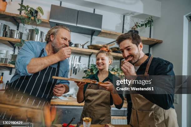 male chefs tasting salami while standing by colleague in kitchen - tasting - fotografias e filmes do acervo