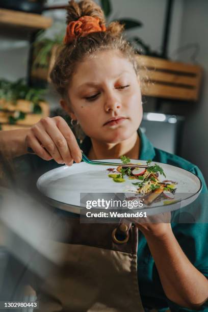 young chef arranging vegetable with tongs in plate while standing in kitchen - chef finishing stock pictures, royalty-free photos & images