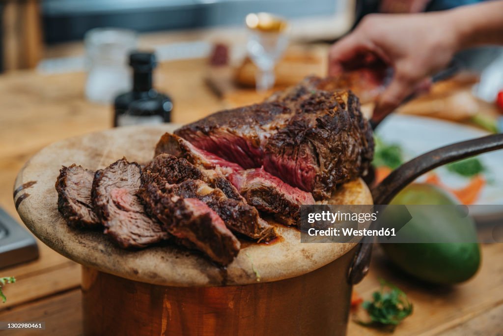 Chef arranging slice of cooked tomahawk steak in wooden plate at kitchen