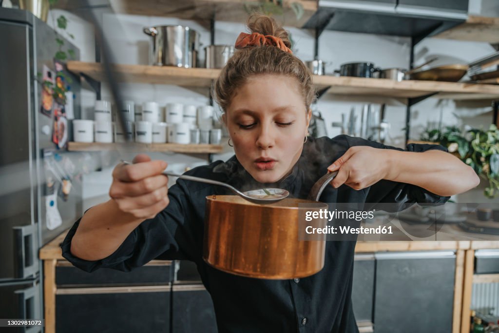 Young female chef tasting Broth soup while standing in kitchen