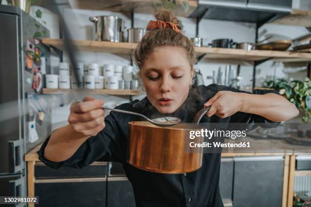 young female chef tasting broth soup while standing in kitchen - 廚師 個照片及圖片檔