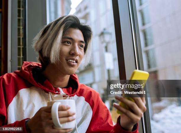 male hipster with smart phone and coffee cup in cafe - asian man long hair stock pictures, royalty-free photos & images