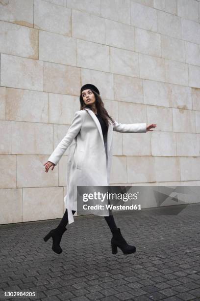 young woman walking by wall on footpath - überzieher stock-fotos und bilder