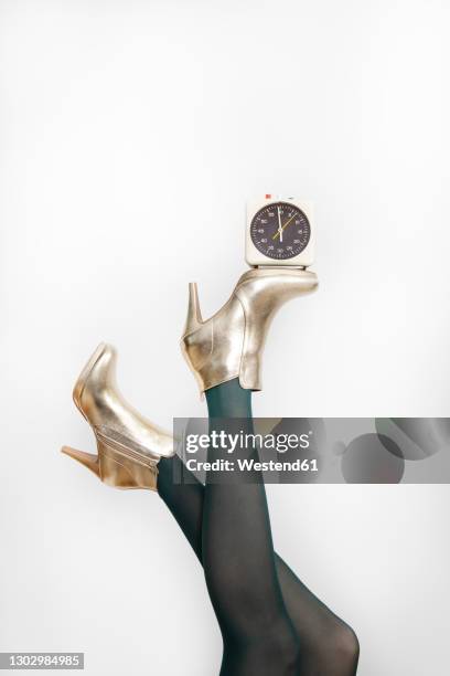 woman wearing golden stilettos while balancing alarm clock against white background - legs in stockings stock pictures, royalty-free photos & images