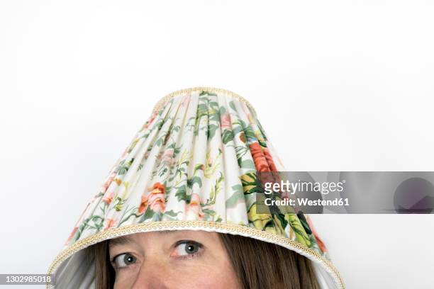 mature woman with lamp shade on head against white background - lamp shade fotografías e imágenes de stock
