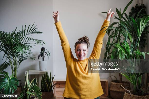 carefree woman with hand raised sitting at home - braccia alzate foto e immagini stock