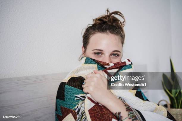 woman wrapped in blanket staring while sitting on bed at home - cold temperature stock-fotos und bilder