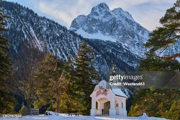 chapel on frozen lakeshore with snow covered mountains in background, bavaria, germany - mittenwald stock pictures, royalty-free photos & images