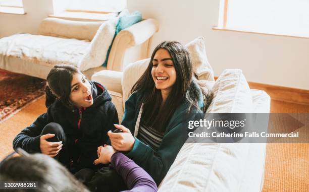 two sisters sit on a sofa with their mum and chat - indian mother daughter stock pictures, royalty-free photos & images