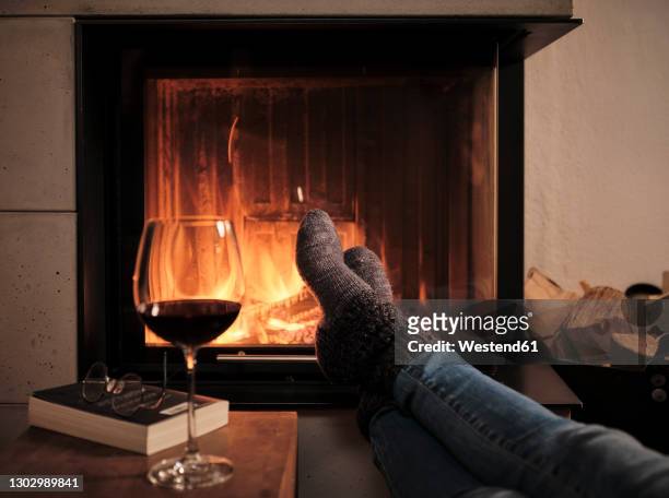woman wearing woolen socks resting feet on table by fireplace at home during winter - fireplace fotografías e imágenes de stock