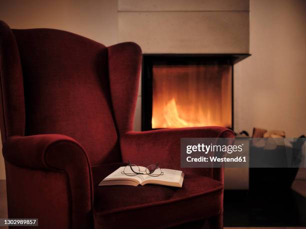 eyeglasses with open book on maroon wingback chair by fireplace at home - fireplace cosy stock pictures, royalty-free photos & images