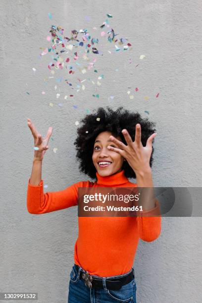 cheerful young woman throwing confetti while standing against wall - wurf oder sprungdisziplin damen stock-fotos und bilder