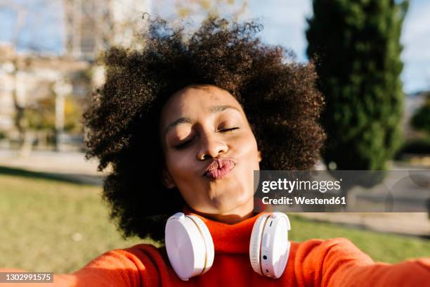 young woman with eyes closed puckering while taking selfie at park - kussmund stock-fotos und bilder