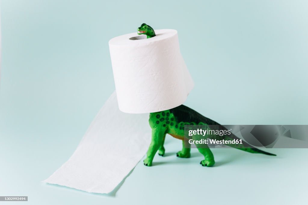 Diplodocus dinosaur toy with a roll of toilet paper around the neck on mint green background