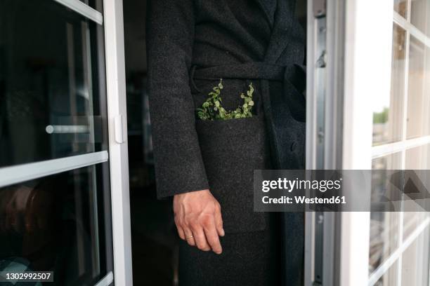 mature man in black coat with plant in pocket standing at doorway - man hands in pockets stock pictures, royalty-free photos & images