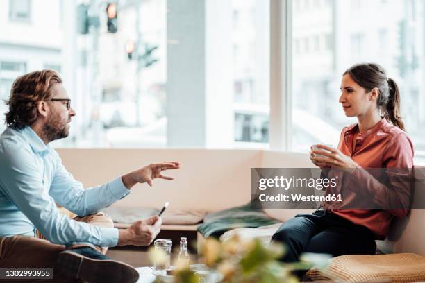 female entrepreneur having coffee while discussing with male colleague at coffee shop - two executive man coffee shop stock pictures, royalty-free photos & images