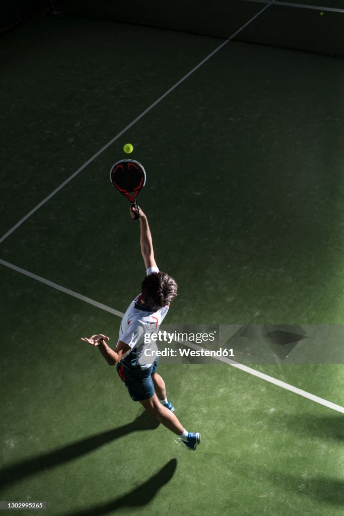 Male athlete servicing ball while playing padel tennis in sports court at night