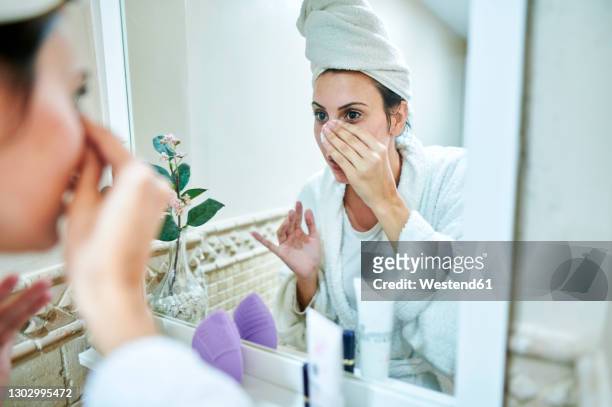 woman removing make-up in front of bathroom mirror - démaquillant photos et images de collection