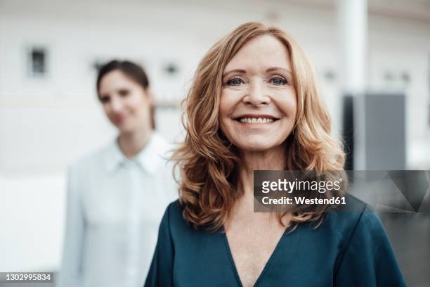 smiling senior woman with female colleague in background at office - mid adult women photos et images de collection