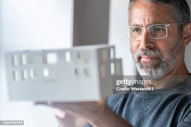 businessman wearing eyeglasses examining architectural model while standing at home - architekt stock-fotos und bilder