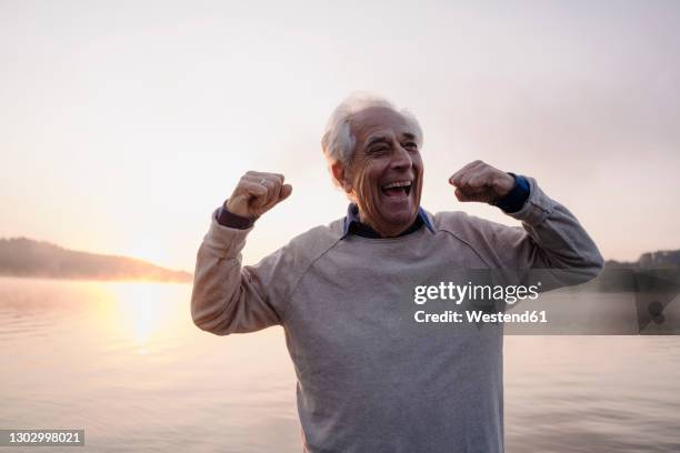 excited man showing bicep while standing against sky - flexes stock pictures, royalty-free photos & images