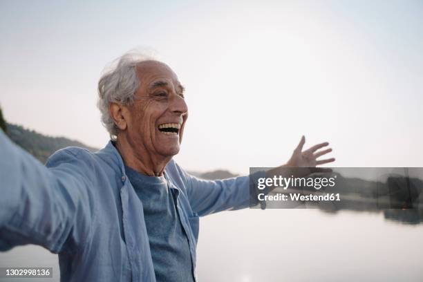 carefree senior man standing with arms outstretched against sky - arms outstretched bildbanksfoton och bilder