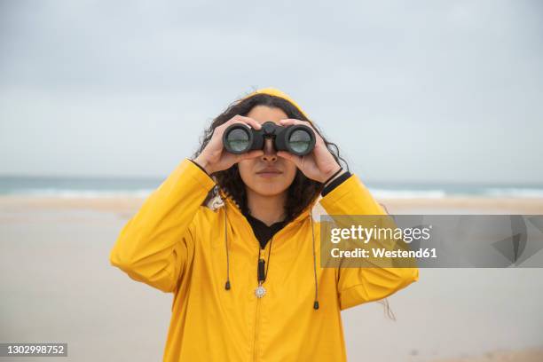 woman using binoculars while standing at beach - canocchiale foto e immagini stock