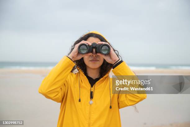 woman using binoculars while standing at beach - binoculars stock pictures, royalty-free photos & images