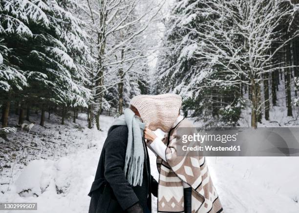 romantic couple covering face with scarf while standing on snow in forest - funny love stock-fotos und bilder