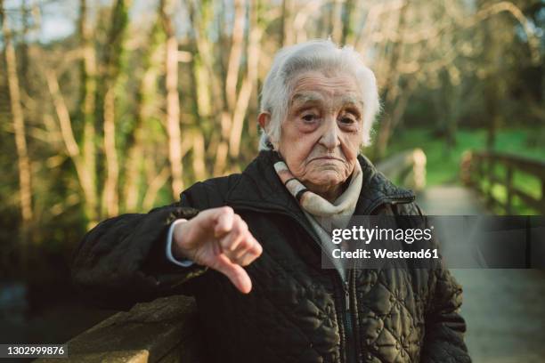 displeased senior woman showing thumbs down gesture during winter - schimpfen stock-fotos und bilder