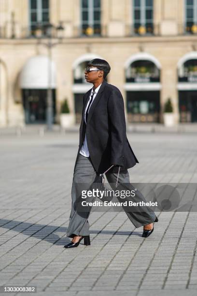 Loïcka Grâce wears sunglasses from Poppy Lissiman, a white long shirt from Levi's, a black t-shirt from Frankie Shop, a gray oversized blazer jacket...