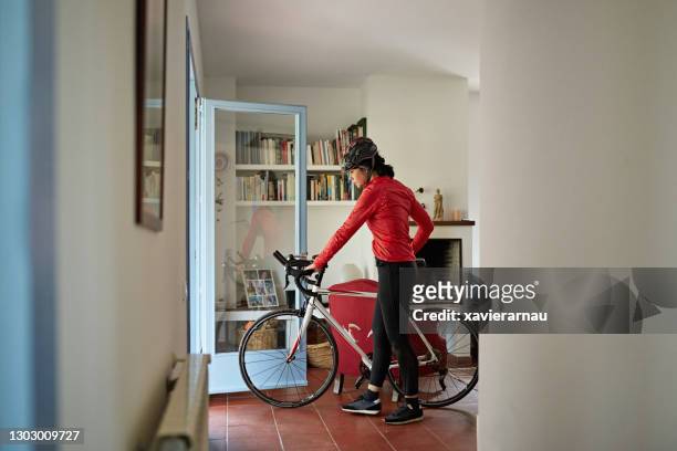 female triathlete walking out of house with racing bicycle - indoor triathlon stock pictures, royalty-free photos & images