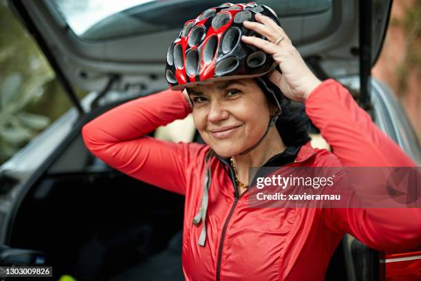 ehrliches portrait von reifen weiblichen radfahrer setzen auf helm - aufsetzen stock-fotos und bilder