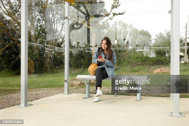 junge studentin wartet auf bus - girl sitting stock-fotos und bilder