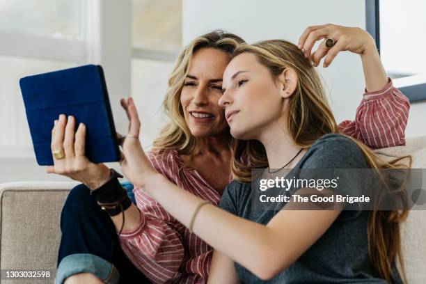 smiling mother and daughter using digital tablet while sitting on sofa at home - familie jugendlicher zufrieden stock-fotos und bilder