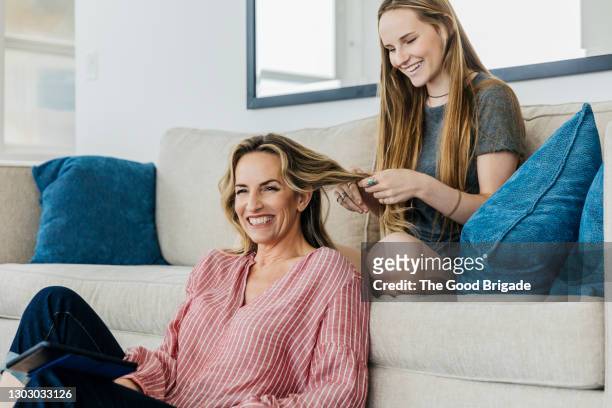 smiling daughter playing with mother's hair while sitting at home - affettuoso foto e immagini stock
