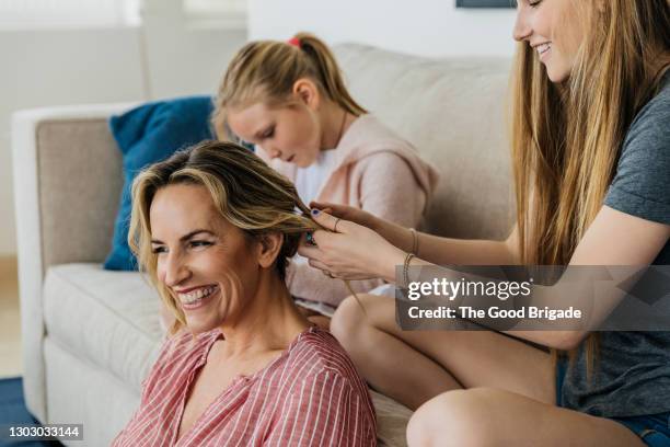 smiling daughter playing with mother's hair on sofa at home - mother daughter couch imagens e fotografias de stock