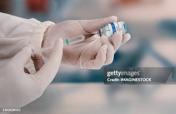 a young doctor in white protective glove is holding a medical syringe and vial - covid 19 vaccine stock pictures, royalty-free photos & images