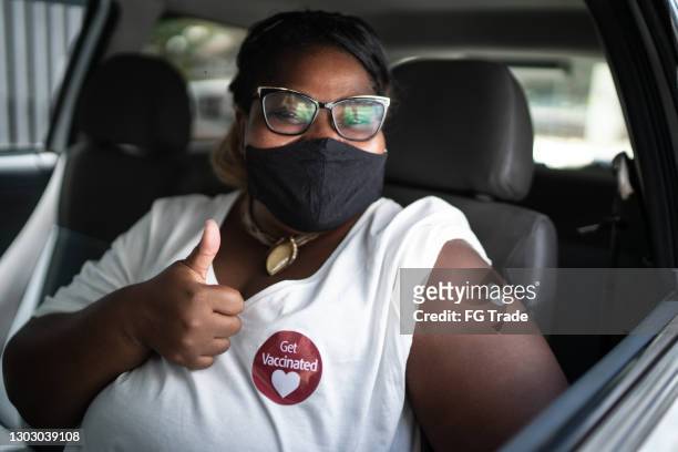 portrait of a happy woman in a car with a 'get vaccinated' sticker - wearing face mask - covid 19 vaccine stock pictures, royalty-free photos & images